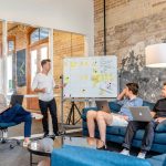 three-men-sitting-while-using-laptops-and-watching-man-beside-whiteboard-scaled
