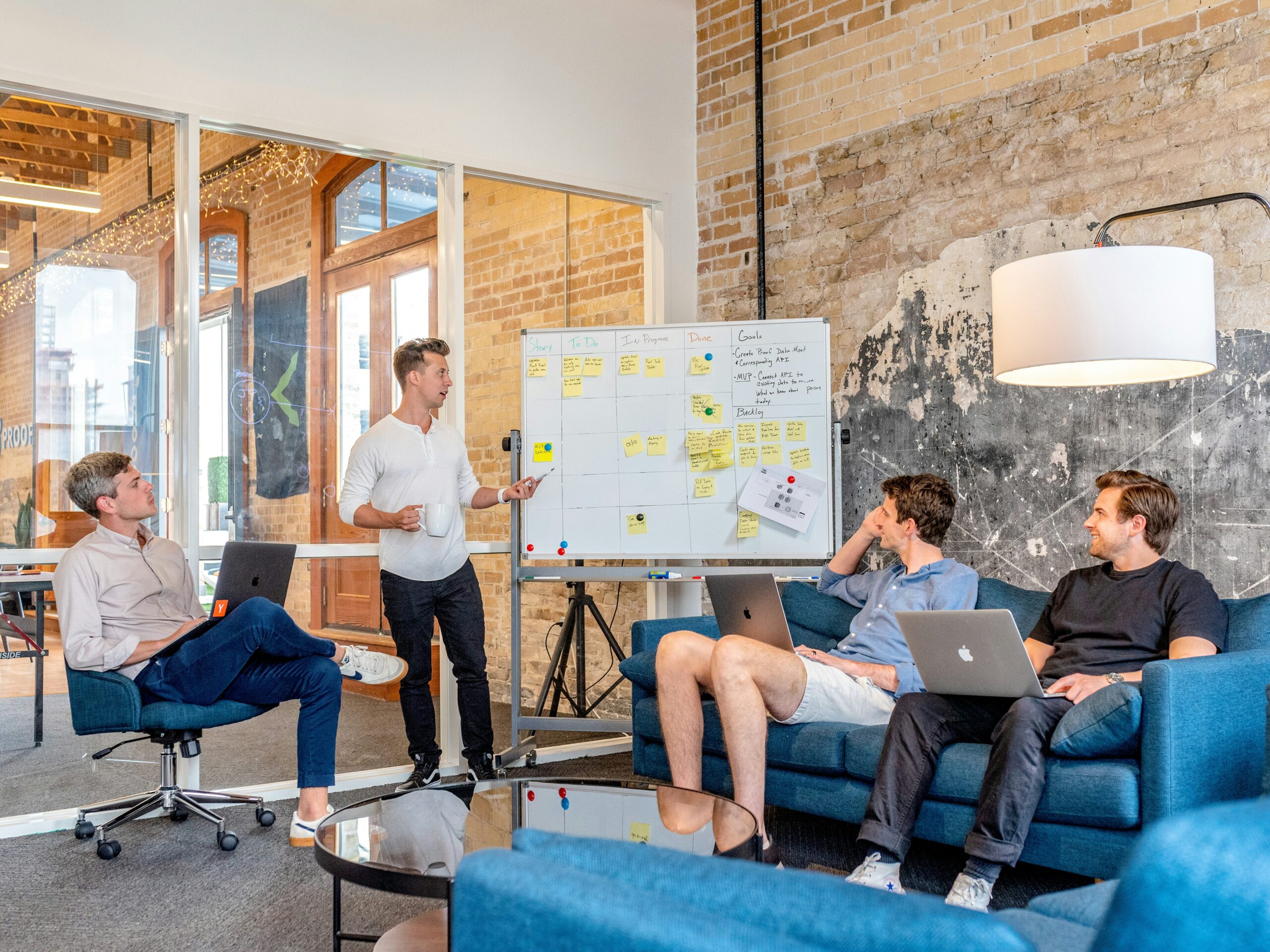 three-men-sitting-while-using-laptops-and-watching-man-beside-whiteboard-scaled